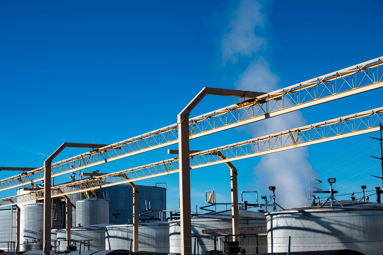 Wide view of an industrial plant with smoke rising from storage tanks against a clear blue sky.